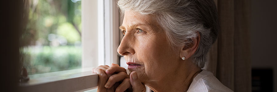Femme âgée regardant par la fenêtre, pensive, la tête posée sur les mains