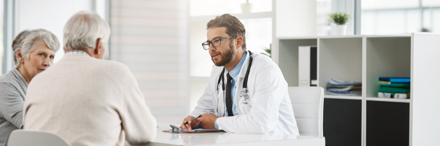 Médecin assis à son bureau qui discute avec un couple de personnes âgées